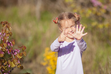 Portrait of a happy cheerful little girl in a purple dress on a background of blooming purple trees, a child walk in the garden with blooming cherries. Girl shows six fingers.