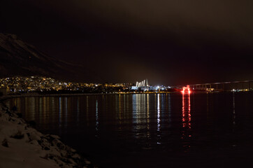 Obraz premium Beautiful firework on night sky in tromsoe city with bridge, cathedral and colorful reflection on the cold fjord water surface on new years eve