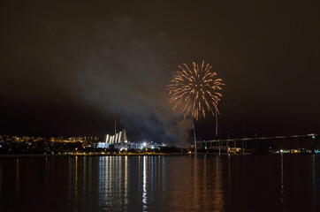 Beautiful firework on night sky in tromsoe city with bridge, cathedral and colorful reflection on the cold fjord water surface on new years eve