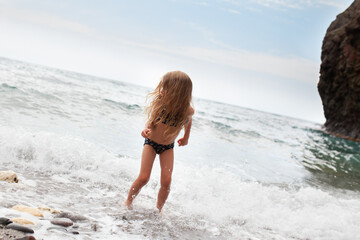 Happy pretty girl walks along the sea coast against the background of the sea, from behind a beautiful landscape