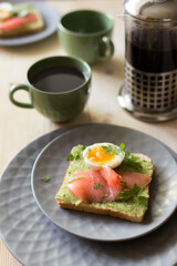 Sandwich with salmon, avocado, and egg on wood table.