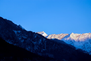 sunrise on the top of a snow-covered mountain. The mountain in the front is covered with pine trees. focus on infinity.