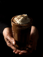 A woman holds a glass of milk chocolate cocktail. Black background.
