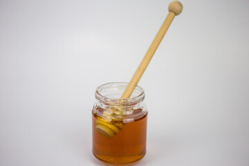 Glass jar with honey and a wooden stick on a white background