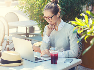 Outdoor photo of woman enjoying free time at cafe table while checking social networks via laptop...