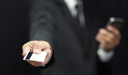 Fototapeta premium Businessman in black suit holding credit card and using smartphone background, Banking concept