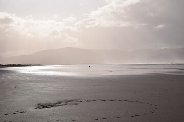 Dramatisches Wetterlage an der irischen Küste. Person läuft durch die goldenen Sonnenstrahlen. Schwarzer Sand und extreme Beleuchtung