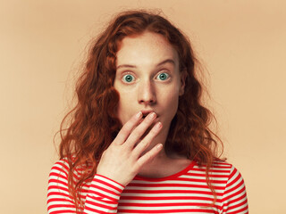 Oh my god! Young redhead girl with eyes wide open with fear or amazement, covering open mouth with palm, isolated on brown background. OMG concept
