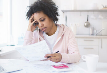 Upset african american woman sitting at kitchen table with laptop, dealing with financial stress...