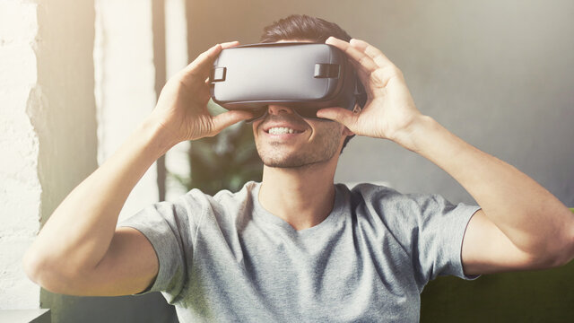 Portrait Of Young Attractive Man Wearing Vr Goggles At Home, Experiencing Virtual Reality Using 3d In Modern Room