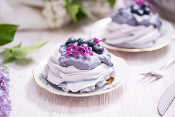 Porcelain plate with meringue with whipped cream decorated with lilac flowers on wooden background