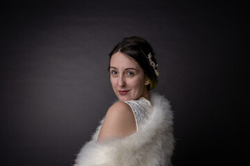 Vintage photo of a young attractive elegant caucasian woman with brown brunette hair and highlighted green hair, wearing a sexy white dress and fur wrap on a black background.