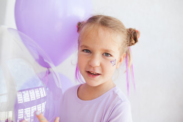Fototapeta premium Portrait of a cheerful pretty girl with purple and transparent balloons, a holiday at the child