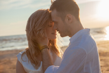 Fototapeta premium Love, romance, walk. Airy portrait of beautiful couple kissing on background of sunset sea, sandy beach and clouds.