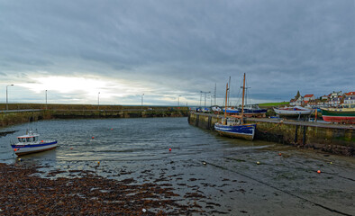 The inner harbour of the small Fishing Village of St Monan's on the Fife Coast, in Winter, with Two boats grounded in the mud at low tide under storm clouds