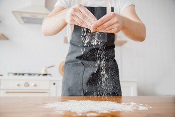 Experienced chef prepares workplace for rolling out dough, sprinkles flour on wooden table, light...
