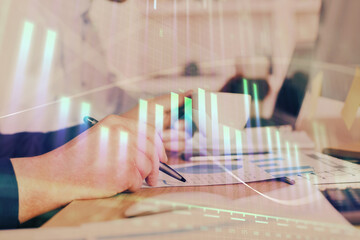 Double exposure of man's hands writing notes of stock market with forex graph.