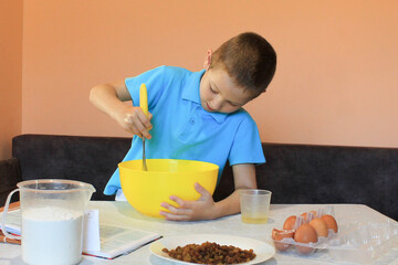 Little boy is preparing cupcakes. Funny and serious schoolboy prepares a dough and makes a delicious dessert. Selective focus