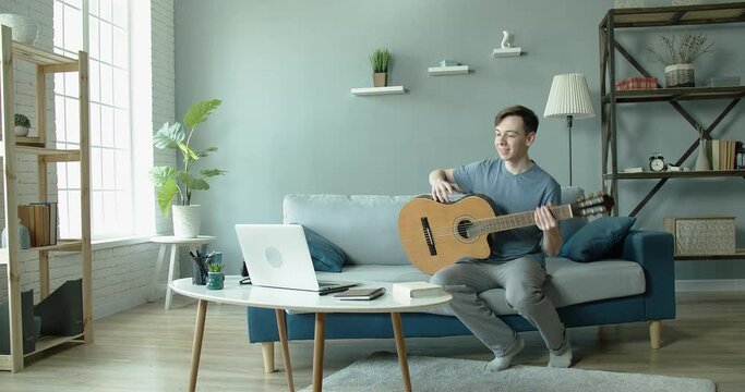 A young man walks into a room with a beautiful interior, says Hello to friends online, and they sing and play guitar together online. Internet communication