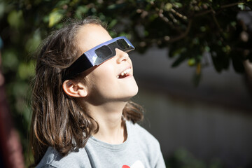 smiling girl watching an eclipse of the sun with eclipse glasses - obrazy, fototapety, plakaty