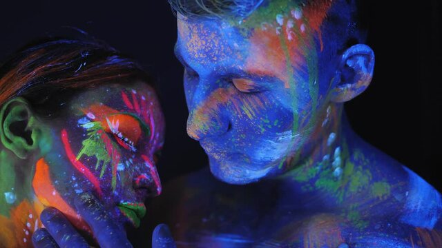 Portrait of a couple with UV drawings on the skin in the dark under the light of fluorescent lamps. Body art on the couple's body glows in neon light.