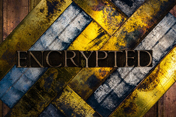 Photo of real authentic typeset letters forming Encrypted text on vintage textured silver grunge copper and gold background
