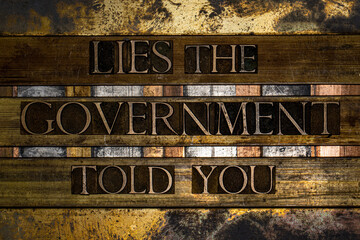 Photo of real authentic typeset letters forming Lies the Government told you text on vintage textured silver grunge copper and gold background