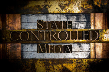Photo of real authentic typeset letters forming State Controlled Media text on vintage textured silver grunge copper and gold background