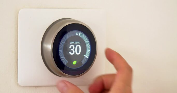A persons hand saving energy during summer high temperatures on centigrade celsius metrics using a smart thermostat on a white wall.