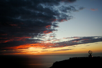 Noth Cape, Norway. View of a red midnight sun in the horizon and the globe with people in the other side.