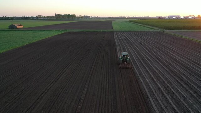 A farmer plowing his field with a tractor during spring, seen from above with a drone.