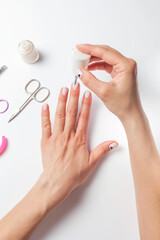 Female hands paint nails, next to lay down devices for nail care. The girl does a manicure. on white background. View from above
