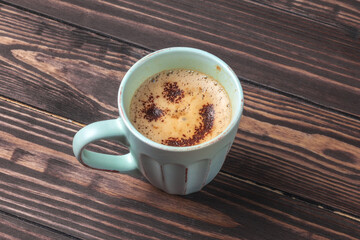 Cup of coffee with emoticon on a foam on a wooden table, top view. A latte or cappuccino with chocolate topping in the form of a smiling face.