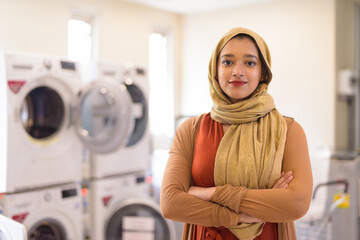 Young beautiful Indian Muslim businesswoman with arms crossed as owner of the laundromat