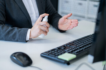 Close-up of female hands office manager at the desk using an antiseptic to disinfect. A woman in a suit treats hands with a sanitizer working at a computer. Mask on the keyboard.