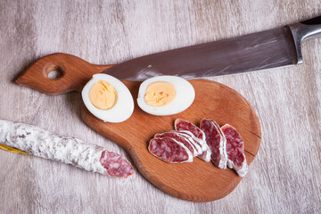 Sliced fuet and cut in half boiled egg on a wooden board