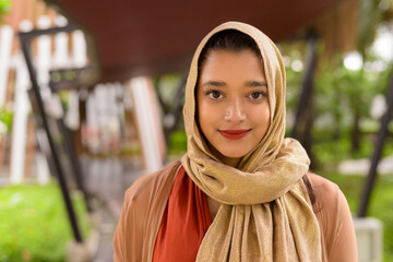Face of young beautiful Indian Muslim woman in the city with nature