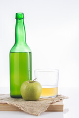 Bottle of Asturian cider with glass and apple on white background.