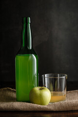 Bottle of Asturian cider with glass and apple on dark background.