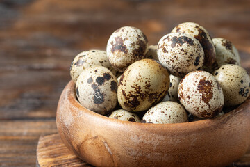 Obraz premium Fresh quail eggs in a wooden bowl on a brown wooden table. Raw quail eggs close-up on a culinary background. Concept of preparation for cooking