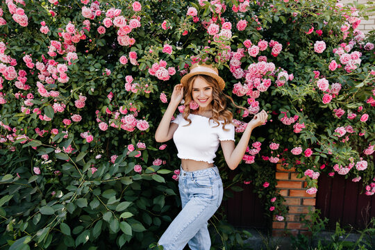 Wonderful girl having fun while resting in garden. Blissful curly woman in jeans enjoying nature views.