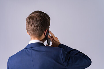 Businessman talking on a mobile phone view from the back. Back view of young man talking on cell phone on the grey background