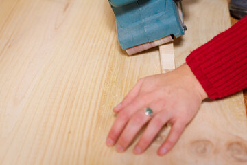 Female hand using a sander on small piece of wood.