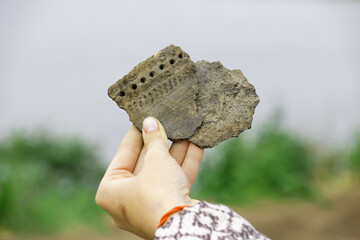 Pieces of ancient clay vessel in the hand of an archaeologist