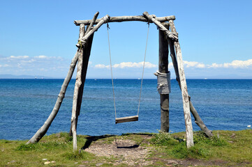 Wooden old swing without people on the background of the Japanese sea on a summer day