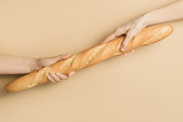 Two women's hands hold a French baguette on a light background