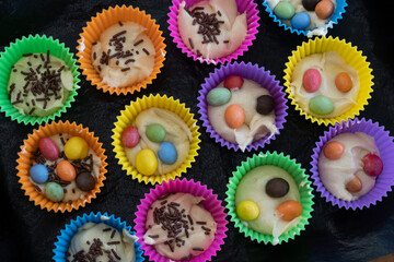 Delicious pastry cooked at home. Homemade cupcakes in multi-colored silicone molds and with colored chocolates inside on a baking tray.