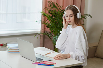 A cute girl is studying online with headphones. On the table is a laptop