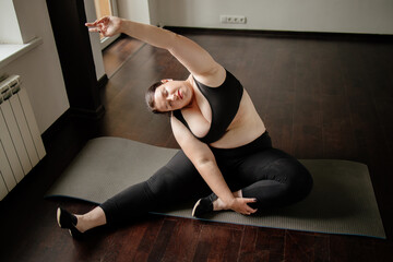 Fitness, home training, flexibility. Overweight woman doing stretching exercises on a fitness mat at her living room. Healthy lifestyle