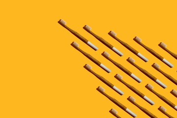 Wedge or arrow shaped bamboo toothbrushes with a white handle and hard shadow on yellow background. Zero waste, eco lifestyle. Biodegradable material.